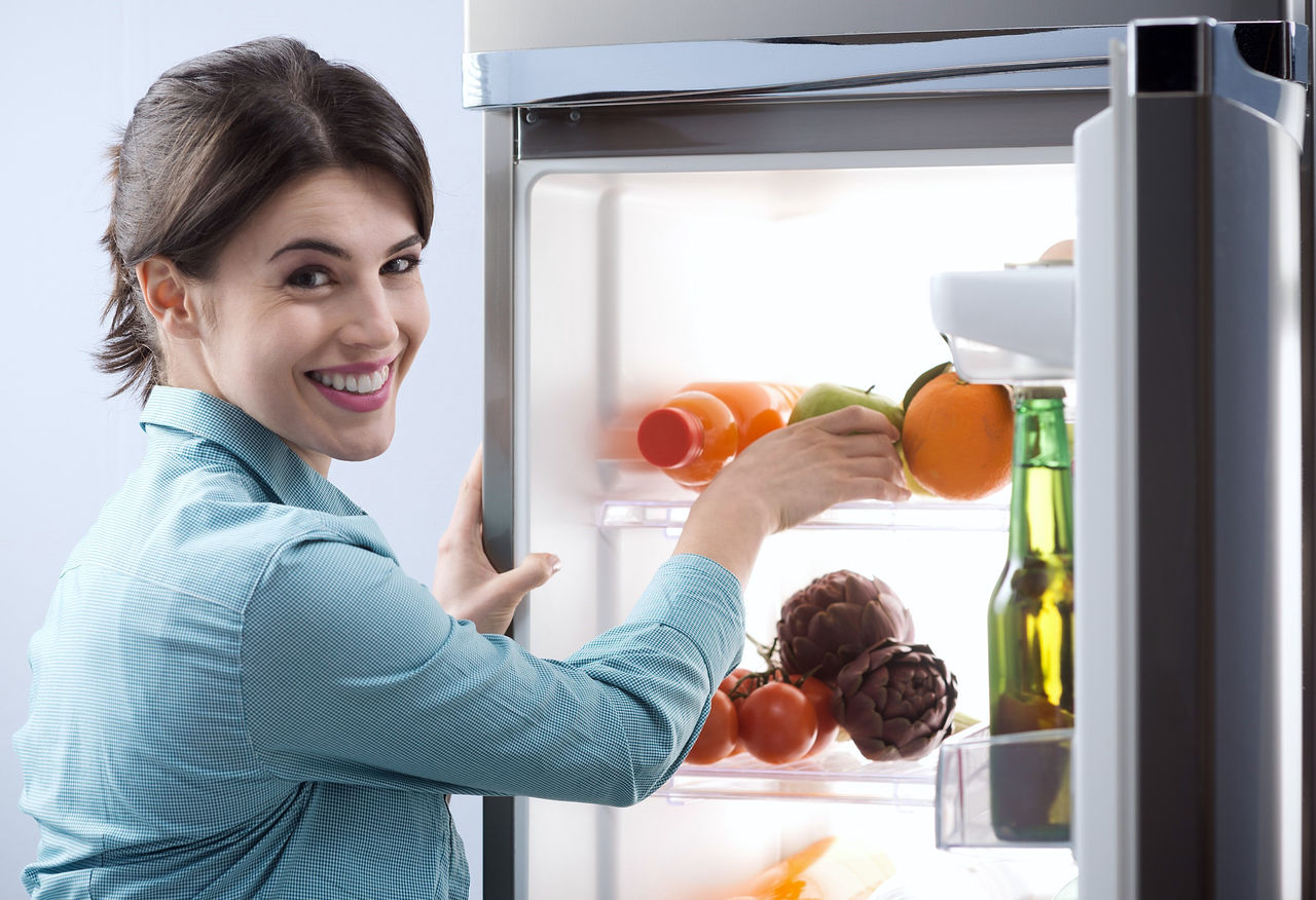 woman next to an open refrigerator which is filled with vegetables
